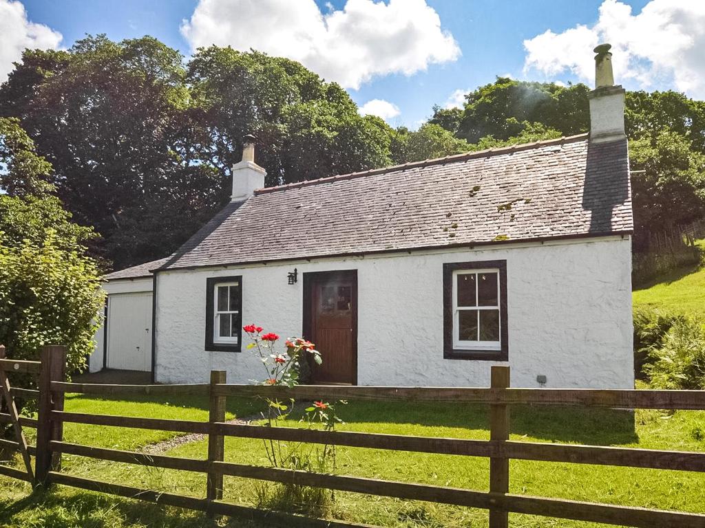 a white cottage in a field with a fence at Professors Cottage in Girvan