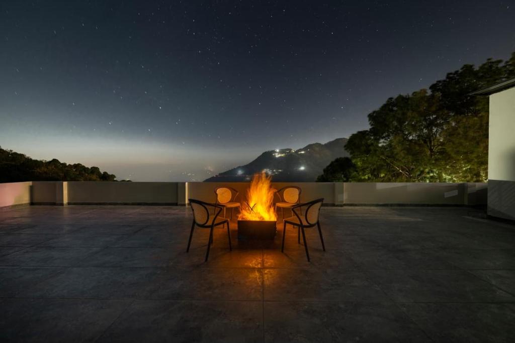 four chairs around a fire on a patio at night at Whispering Woods Homestay Kasauli !! in Kasauli