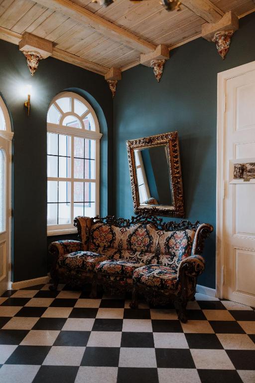 Patterned floral sofa under arched windows, checkerboard floor and ornate framed mirror.