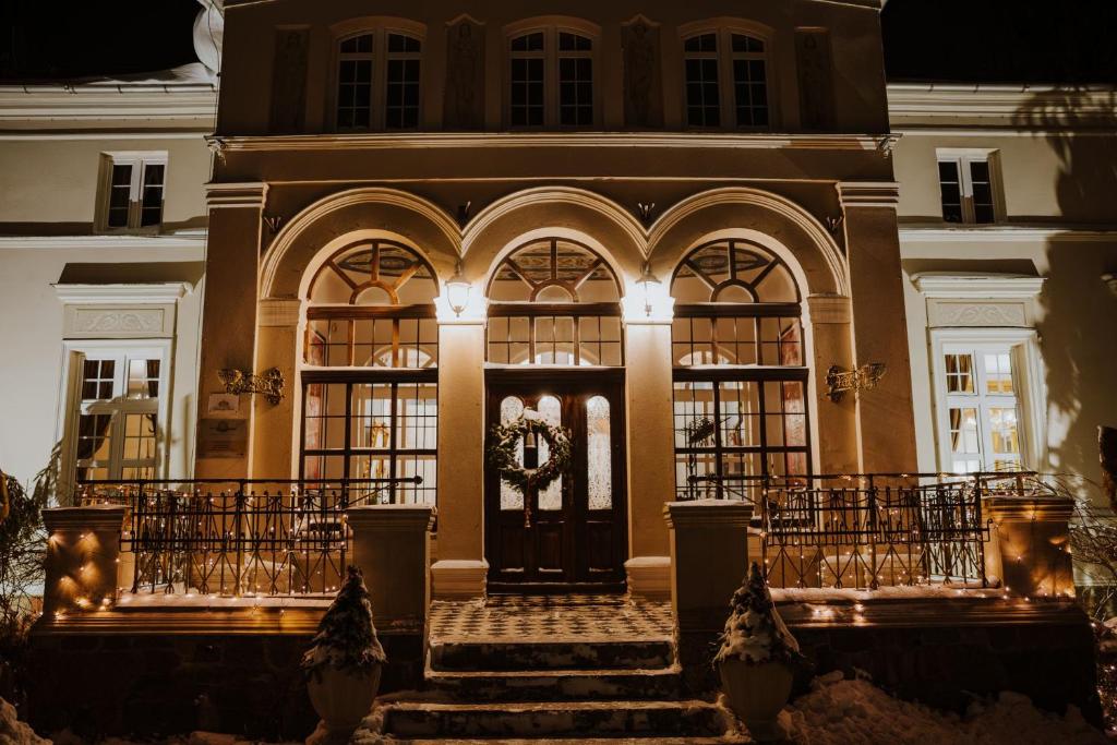 Grand lit building entrance at night with arched windows, wreathed door and snow-dusted steps.
