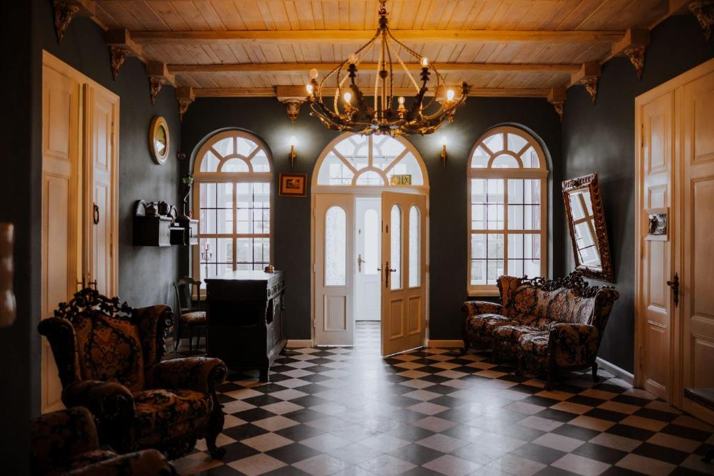 Spacious foyer with chandelier, arched windows, checkerboard floor, floral sofas and soft natural light.