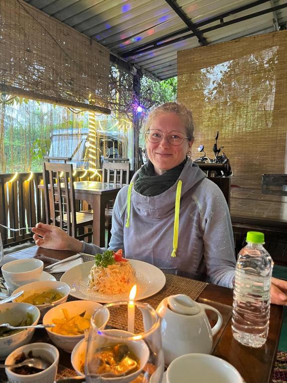 a woman sitting at a table with a plate of food at Ella Nature Life Guest & Restaurant -Free Pickup from Ella in Ella