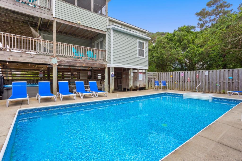 a swimming pool with blue chairs and a house at 2000 - Pipers Paradise in Duck
