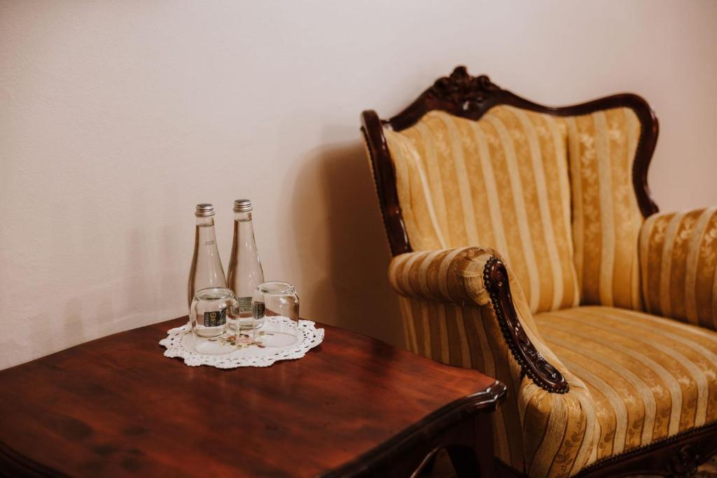 Two glass water bottles and glasses on wooden table beside ornate striped armchair.