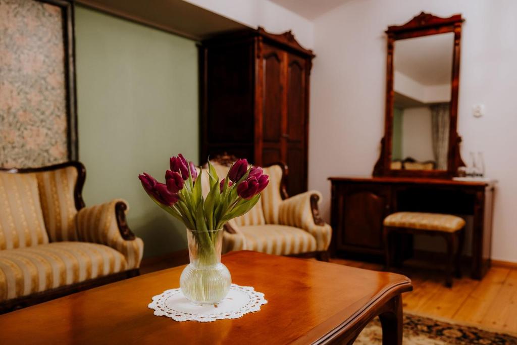Purple tulips in glass vase on wooden table, vintage sitting room with upholstered armchairs and mirror.