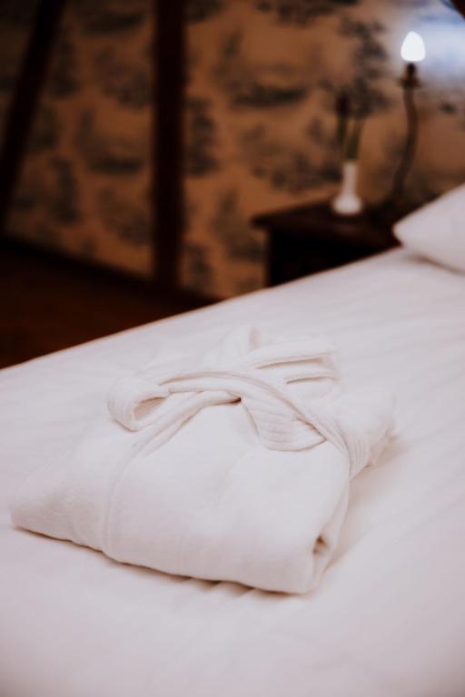 White folded bathrobe placed on crisp bed linens, warm bedside lamp and patterned wallpaper background.