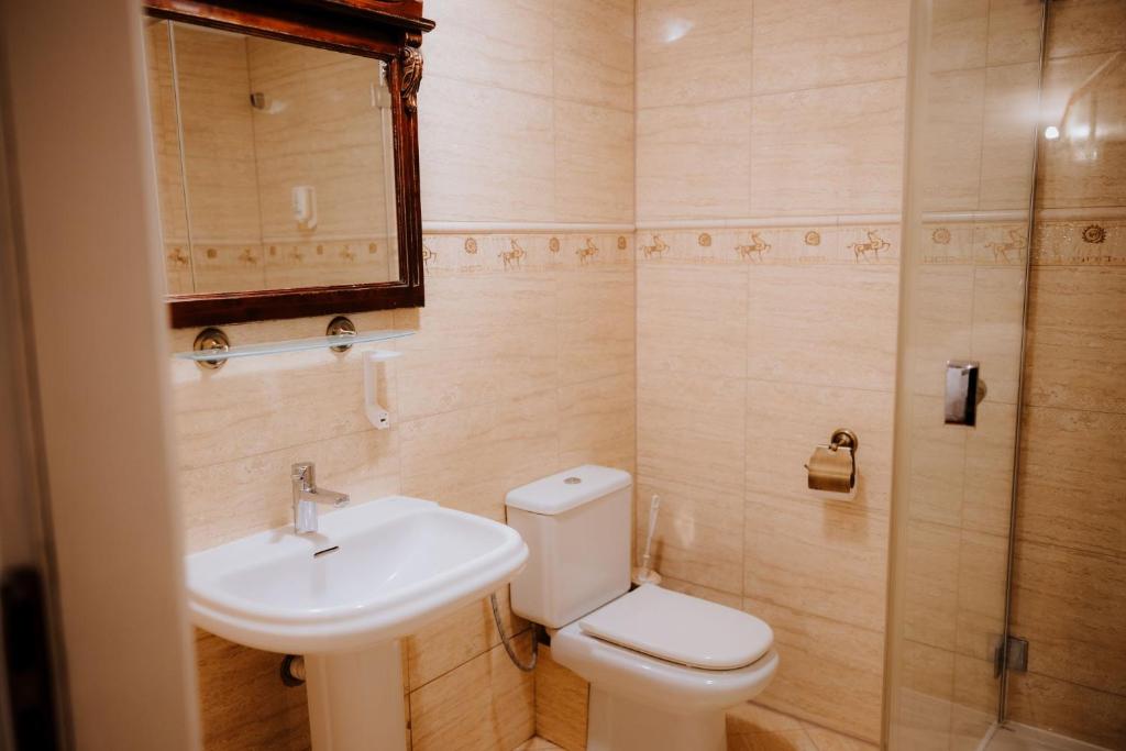 Small modern bathroom with toilet, pedestal sink, glass shower door, and tiled cream walls.