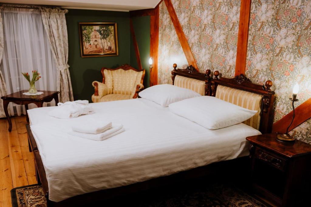 Bright double bed with folded towels and robe, floral wallpaper and cozy armchair.