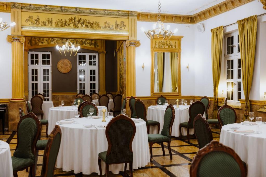 Elegant dining room with round white-clothed tables, green chairs and golden architectural details.
