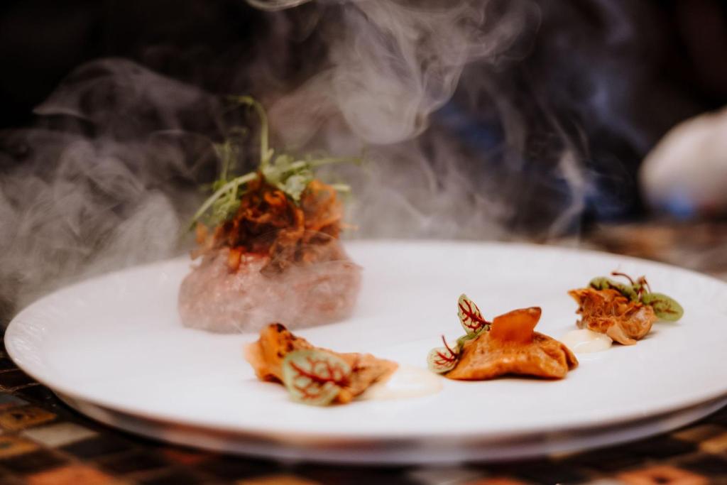 Steaming plated appetizer with three small dumplings and a smoky meat mound, elegant plating.