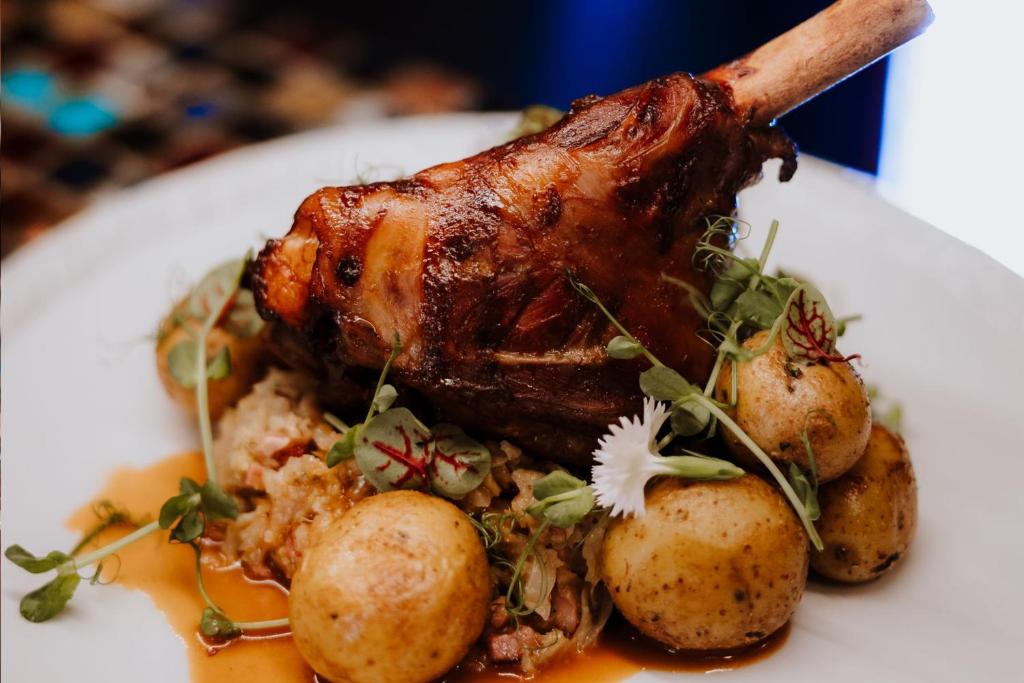 Roasted meat shank and baby potatoes arranged with microgreens and jus on white plate.