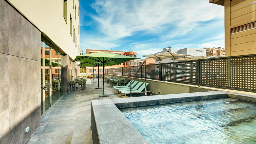 a balcony with a pool with chairs and an umbrella at Sercotel Barcelona El Prat in El Prat de Llobregat
