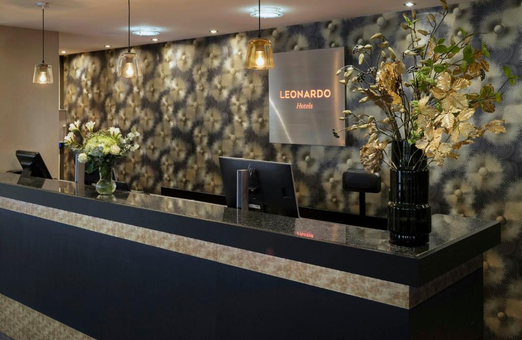 a lobby with a reception desk with flowers on the wall at Leonardo Hotel Hamburg City Nord in Hamburg