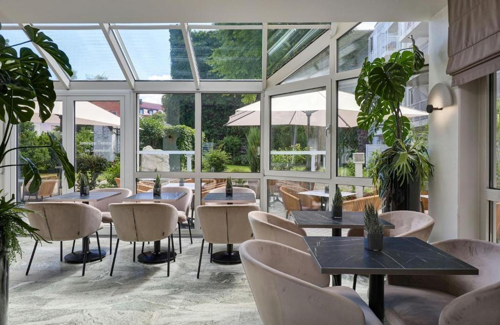 a restaurant with tables and chairs and windows at Leonardo Hotel München City West in Munich