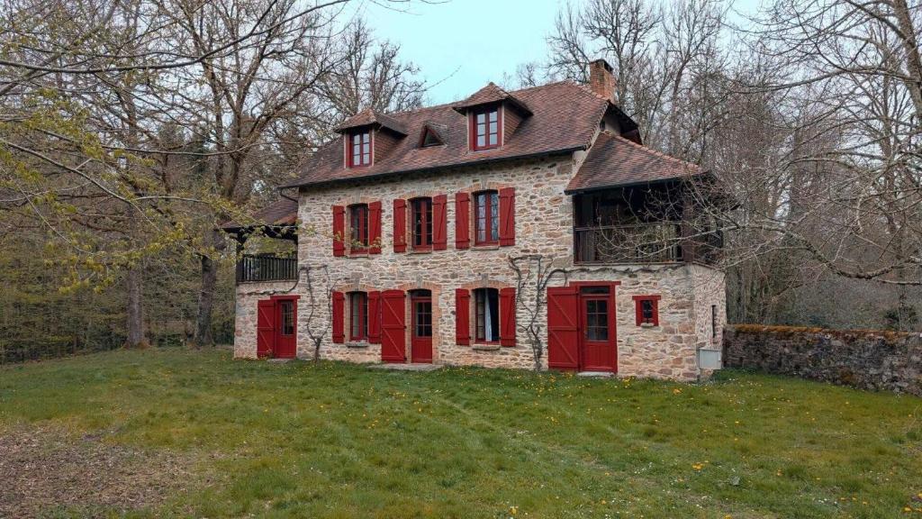 an old stone house with red shutters on a field at Maison des bois in Château-Chervix