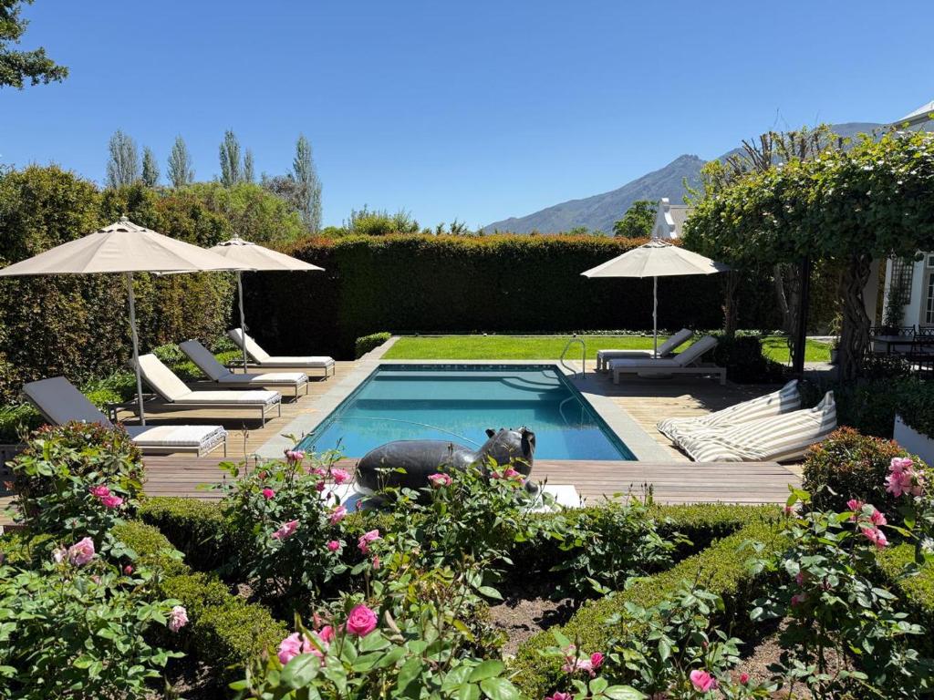 a swimming pool with chairs and umbrellas in a garden at Le Bas De Laine in Franschhoek