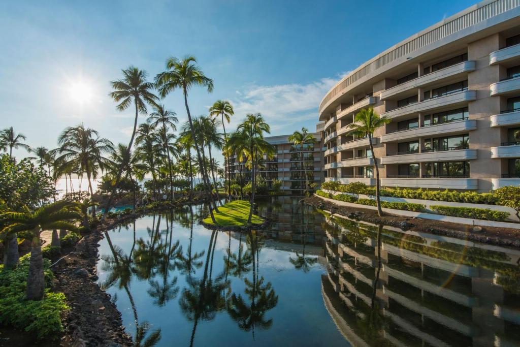 an exterior view of a hotel with palm trees and a pool at Hilton Grand Vacations Club Ocean Tower Waikoloa Village in Waikoloa