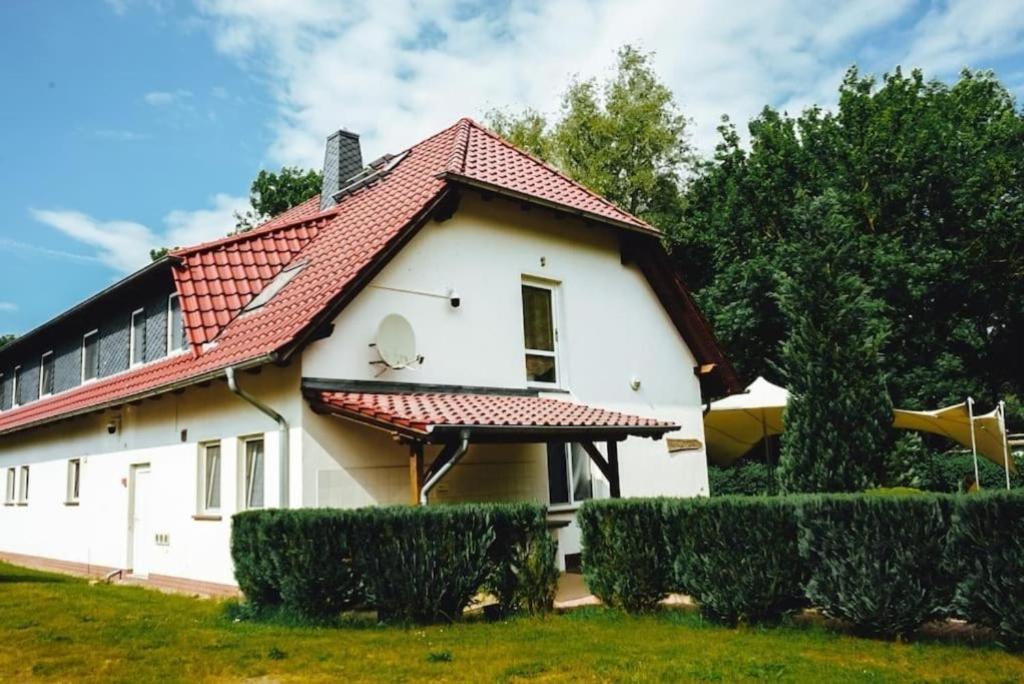 a white house with a red roof and some bushes at Ferienzimmer direkt am See in Priepert