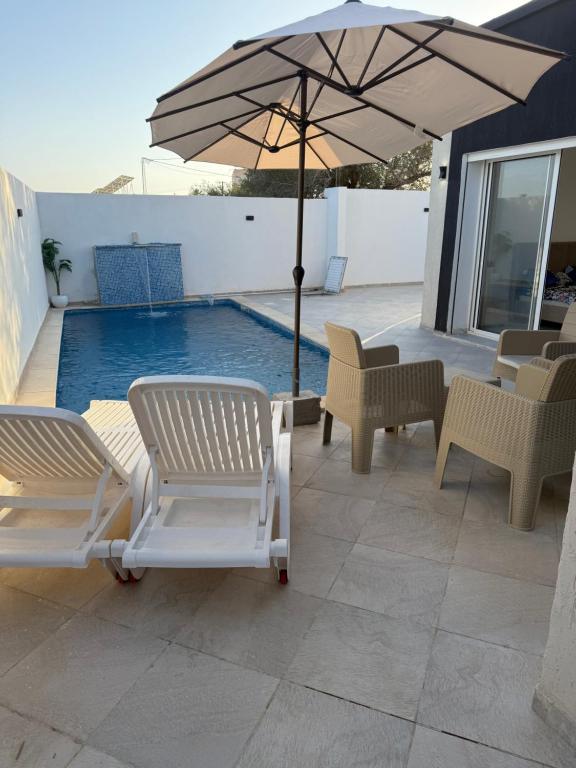 two chairs and an umbrella next to a swimming pool at Villa alnaser in Awlād ‘Umar