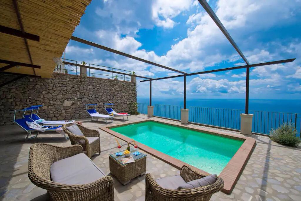 a swimming pool with chairs and a patio with the ocean at House Teresa - private pool in Praiano