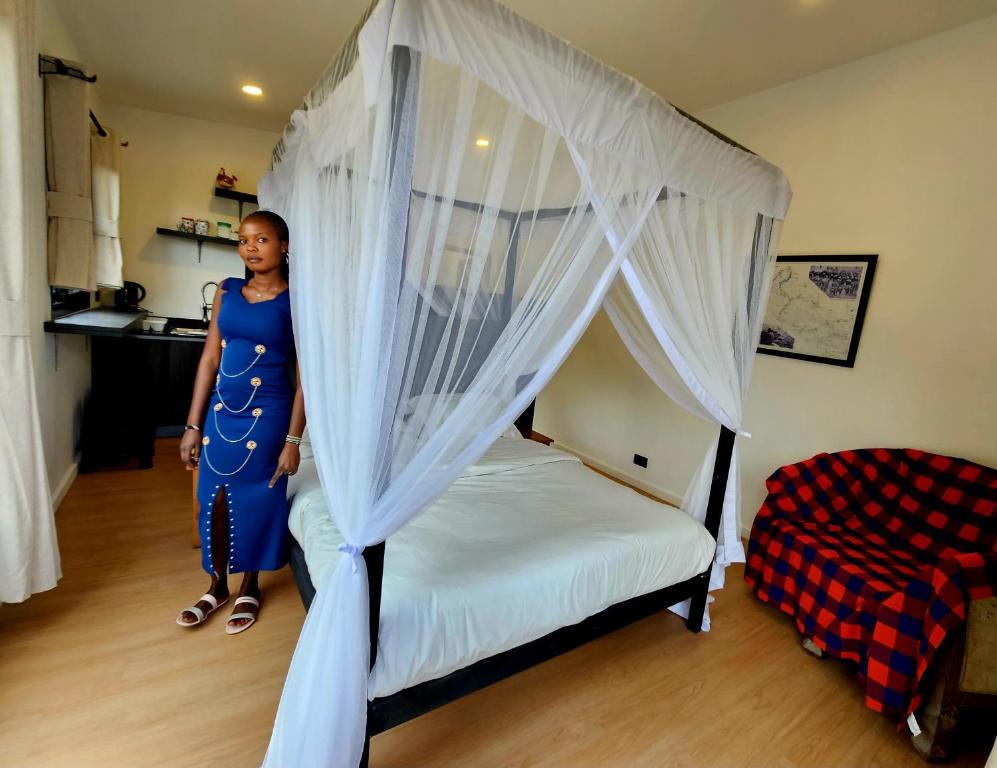 a woman in a blue dress standing next to a bed at MaraRiver TreeHouse in Musiara Campsite