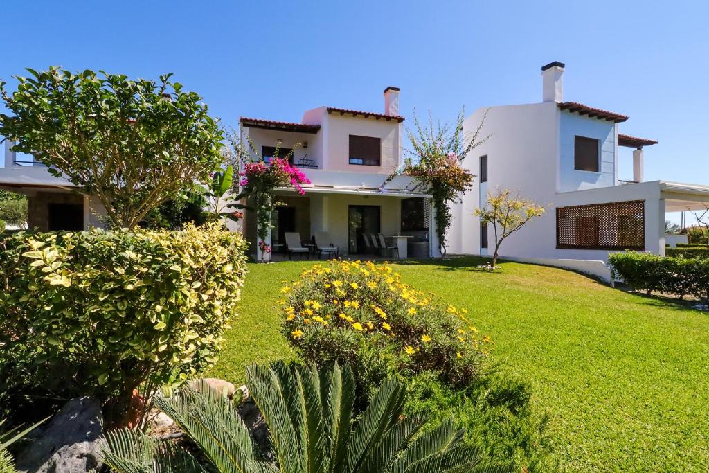 a large white house with a yard with flowers at Sandra Villa Nea Skioni several steps from the sea in Nea Skioni