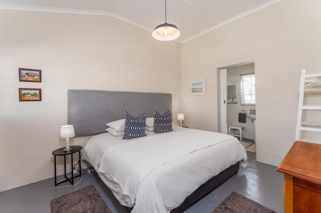 a white bedroom with a large bed with blue pillows at Honeyrock Cottages in Kleinmond
