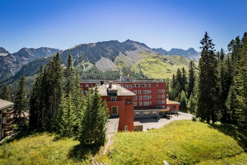 a large red building with mountains in the background at Blatter's Arosa Hotel & Bella Vista SPA in Arosa