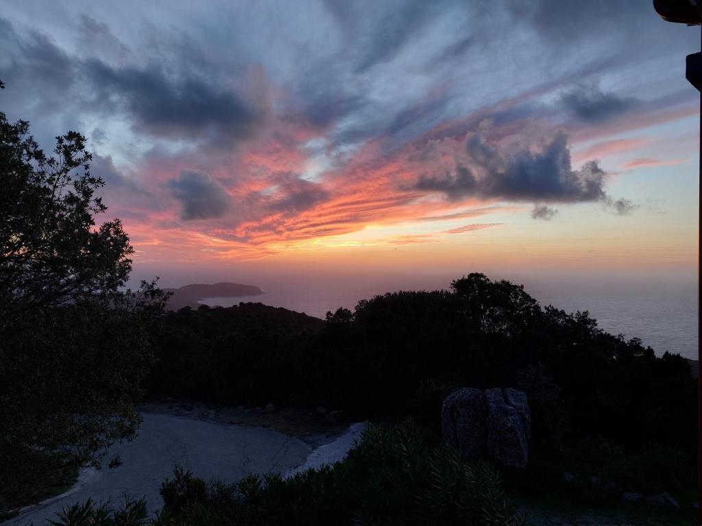 a sunset over the ocean with trees and clouds at Hôtel restaurant Le Belvedere De Coti in Coti-Chiavari