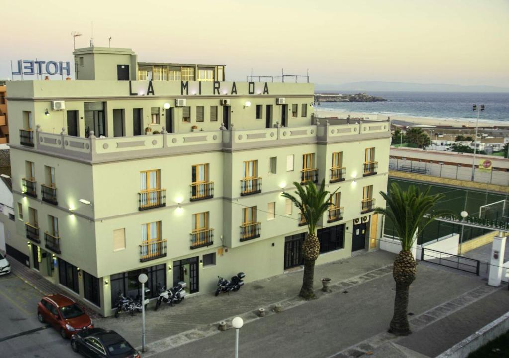 a large white building with palm trees in front of the ocean at Hotel La Mirada in Tarifa