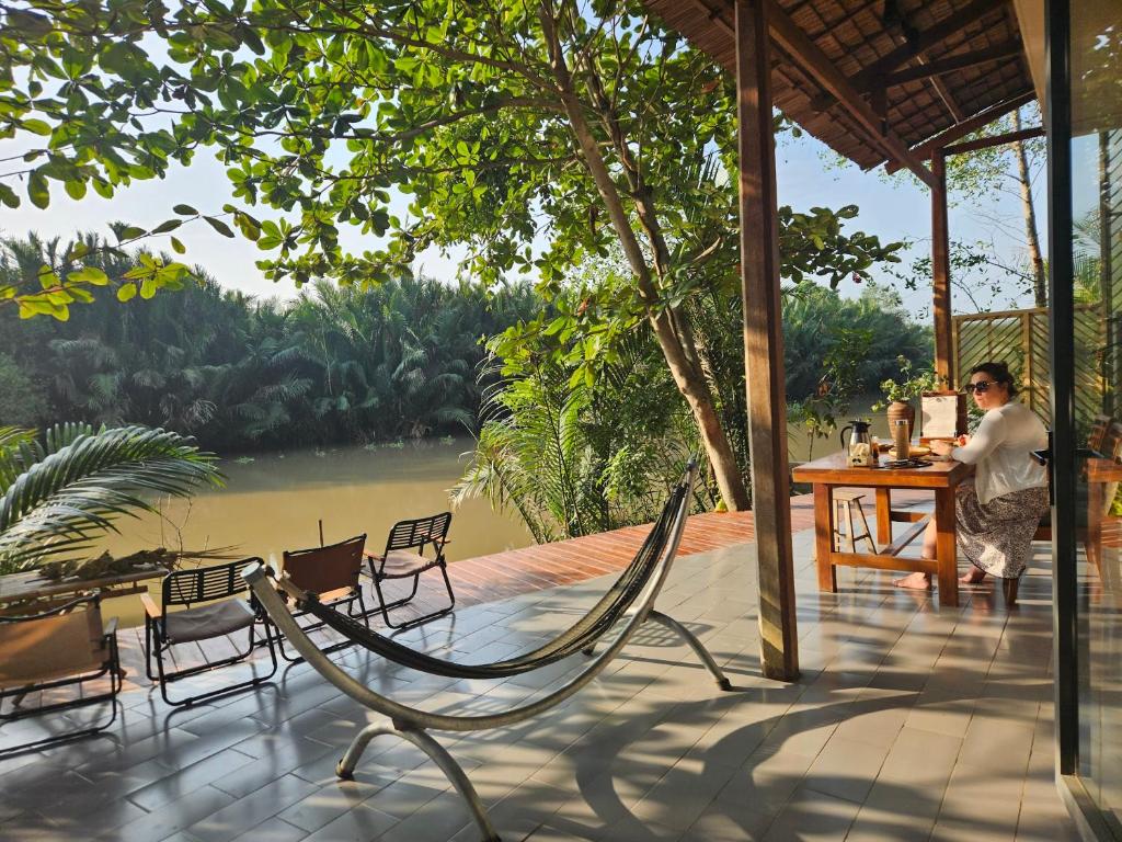 a man sitting at a table on a deck with chairs at Comfy room - InnerZen Mekong Riverside homestay Ben Tre in Ben Tre