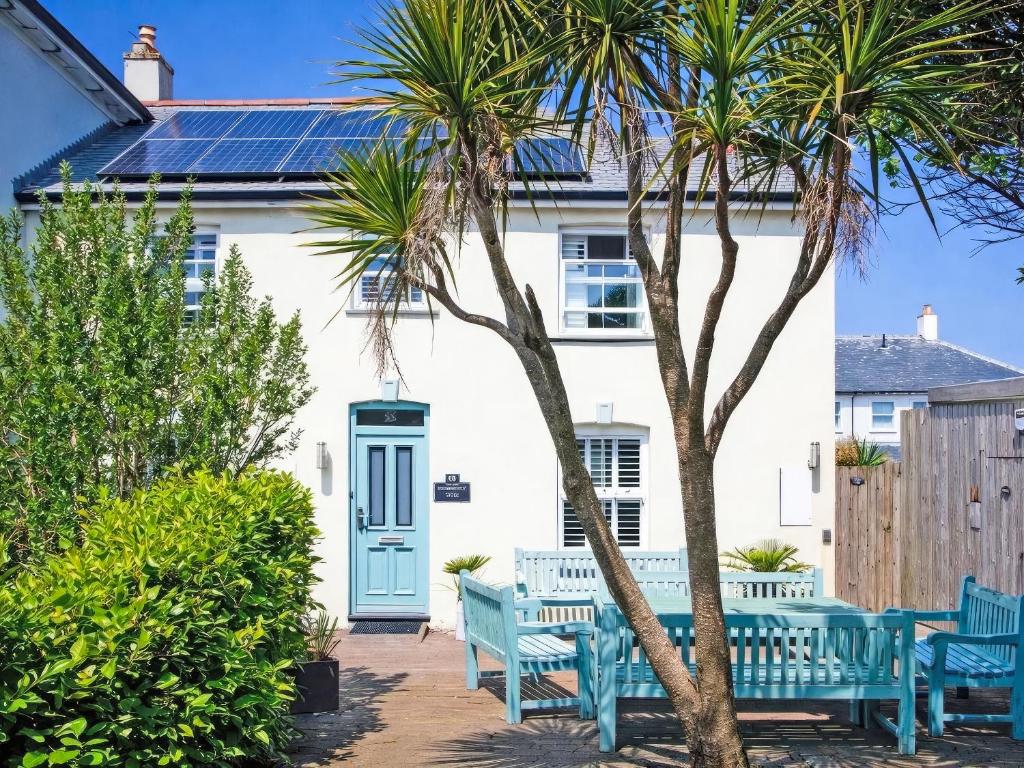 a white house with blue benches and palm trees at Headland Views in Newquay