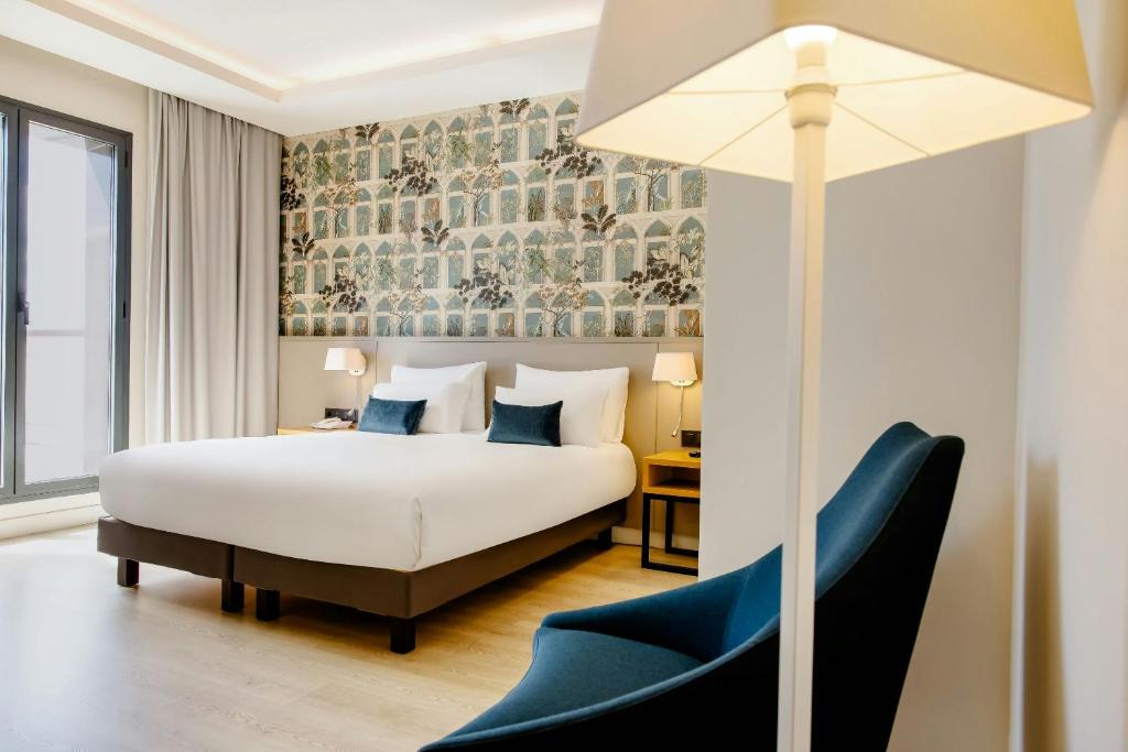 a bedroom with a white bed and a blue chair at Motel One Madrid-Plaza de España in Madrid