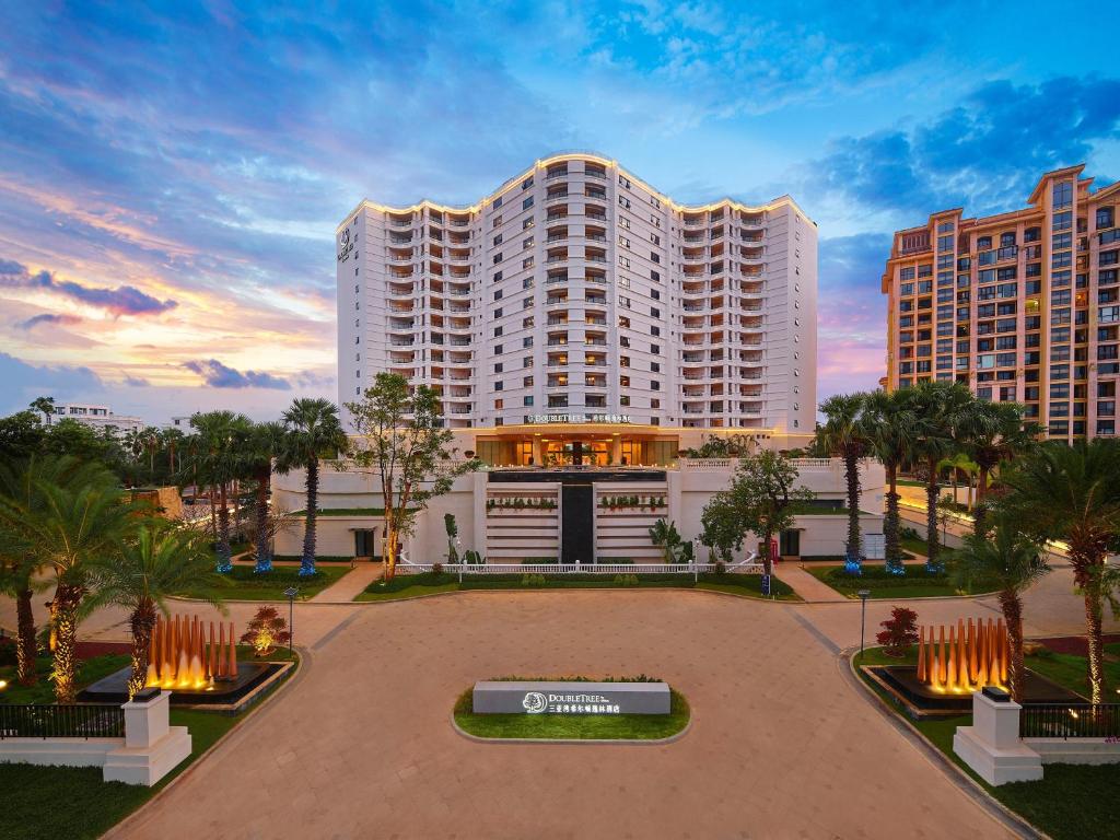 a large white building with palm trees in front of it at Doubletree By Hilton Sanya Bay in Sanya