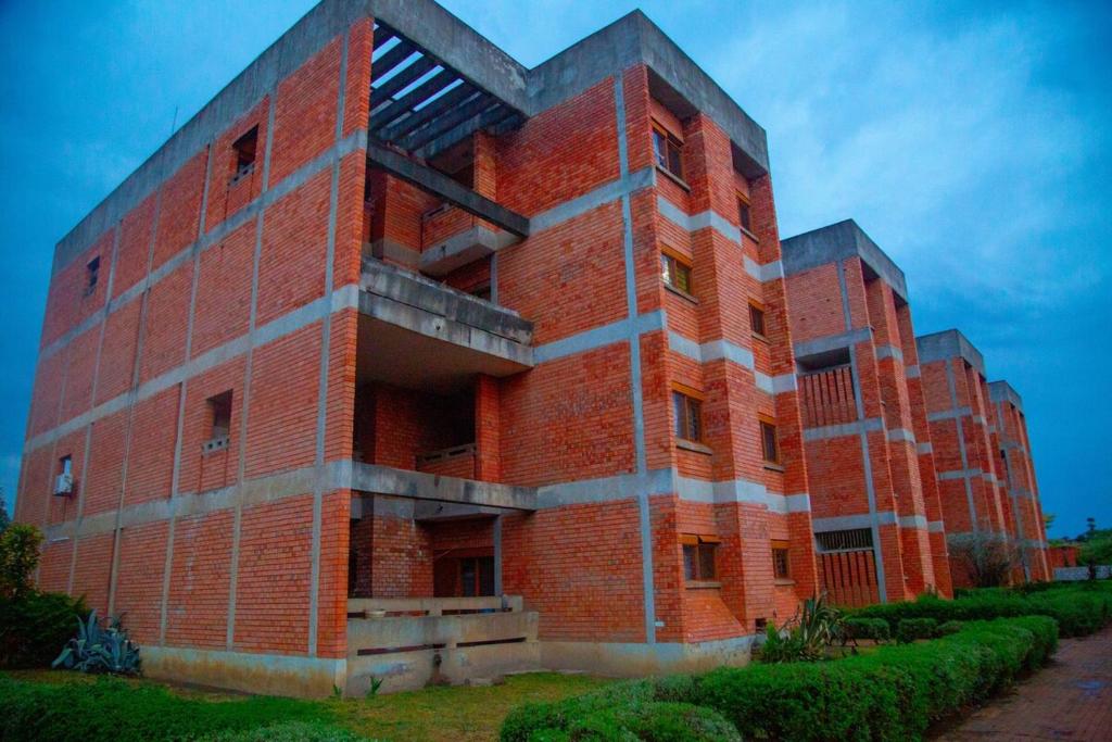 a red brick building with bushes in front of it at Wangu Urban in Mpemba