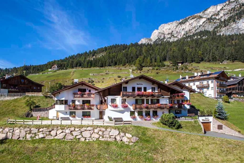 a building on a hill with mountains in the background at Hotel Garni Morene in Selva di Val Gardena