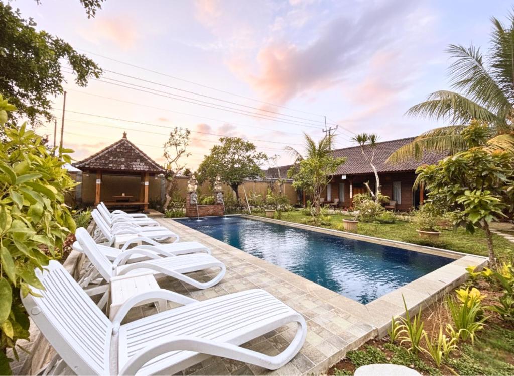 a row of white lounge chairs next to a swimming pool at Buana Sari Villas by AGATA in Bangli