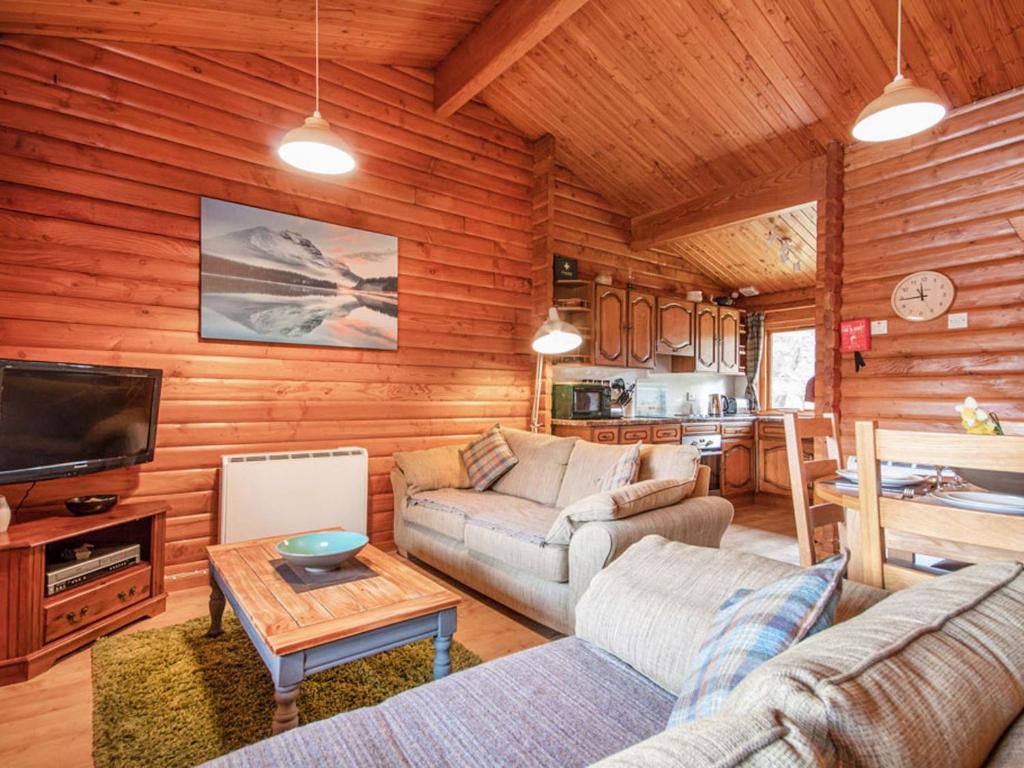a living room with a couch and a tv in a cabin at Lochside Log Cabin in Brora