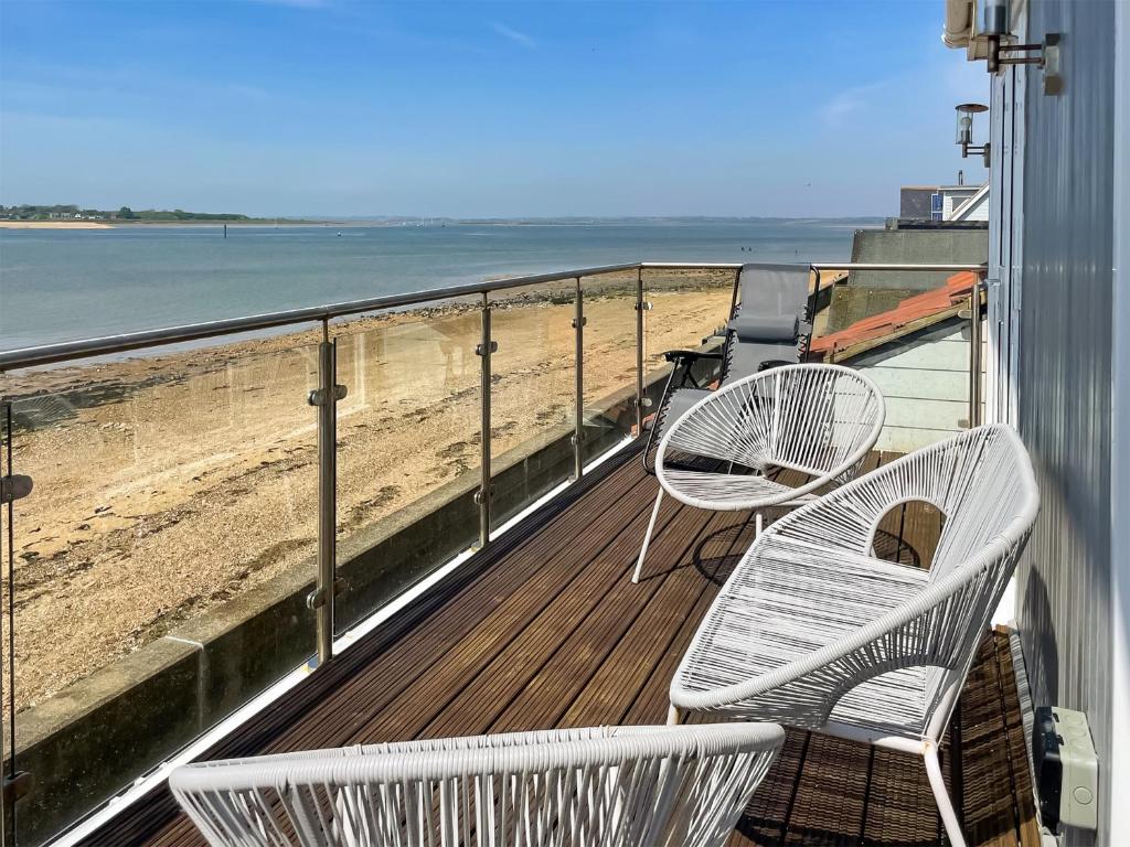 two white chairs sitting on a balcony overlooking the beach at Point Clear View in Brightlingsea