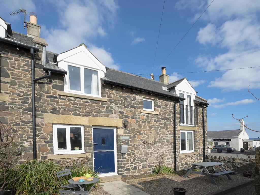 an exterior view of a stone house with a blue door at Cuthbert Cottage in Craster