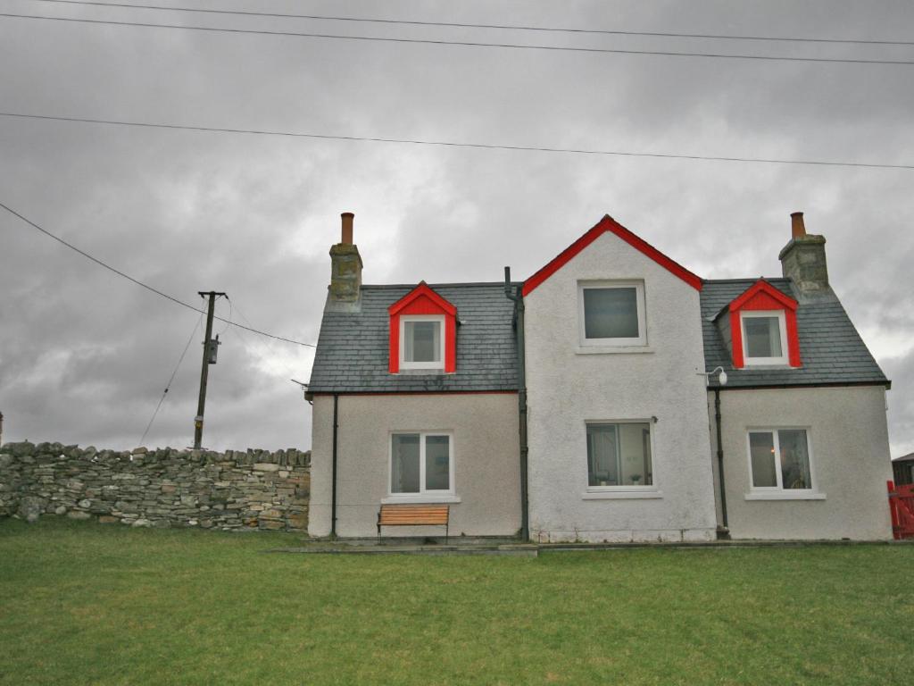 a white house with red windows and a stone wall at Melness Cottage in Melness