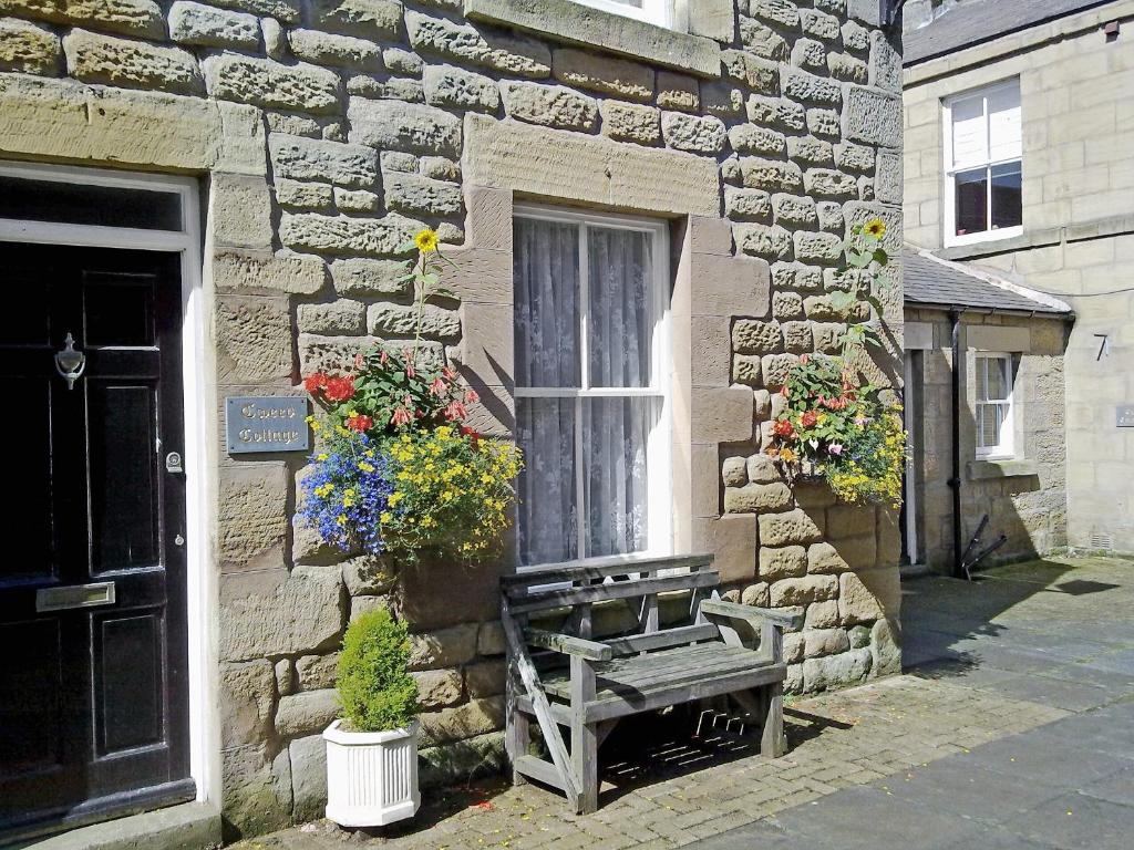 a bench sitting outside of a stone building with flowers at Tweed Cottage in Alnwick