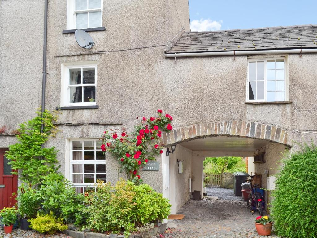 a brick house with an archway with red flowers at Brock Cottage in Broughton in Furness
