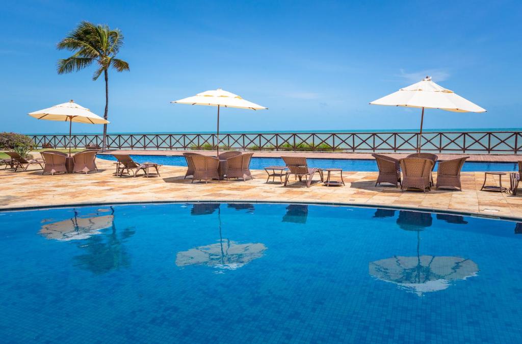 a swimming pool with chairs and umbrellas and the ocean at Cumbuco Dream Village Beachfront in Cumbuco