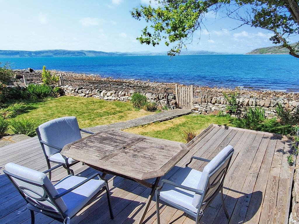 a wooden table and chairs on a deck with the ocean at Sanctuary Cottage in Applecross