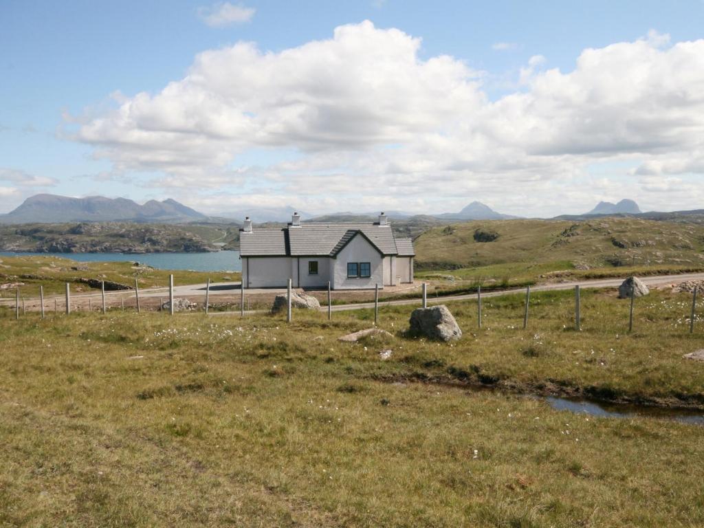 a house in a field next to a body of water at Taigh Uaine in Culkein
