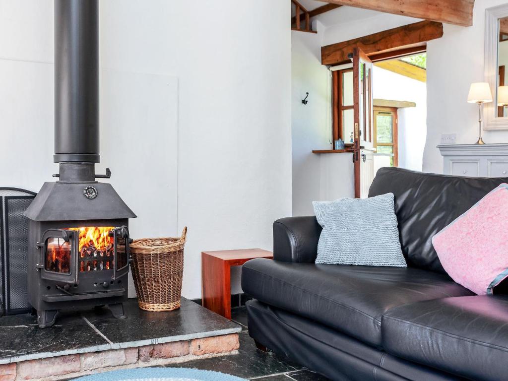 a living room with a black leather couch and a wood stove at Old Dairy in Chulmleigh