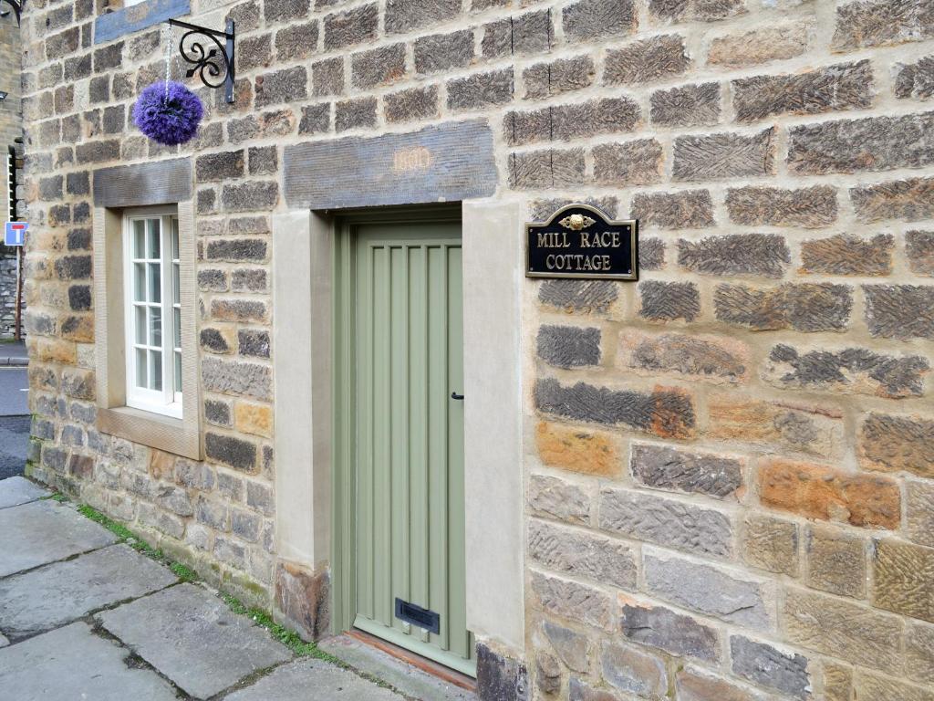 a green door in a brick wall with a sign at Mill Race Cottage in Bakewell