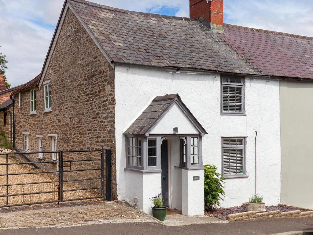 a white house with a black roof and a gate at Hurst Cottage in Sturminster Newton