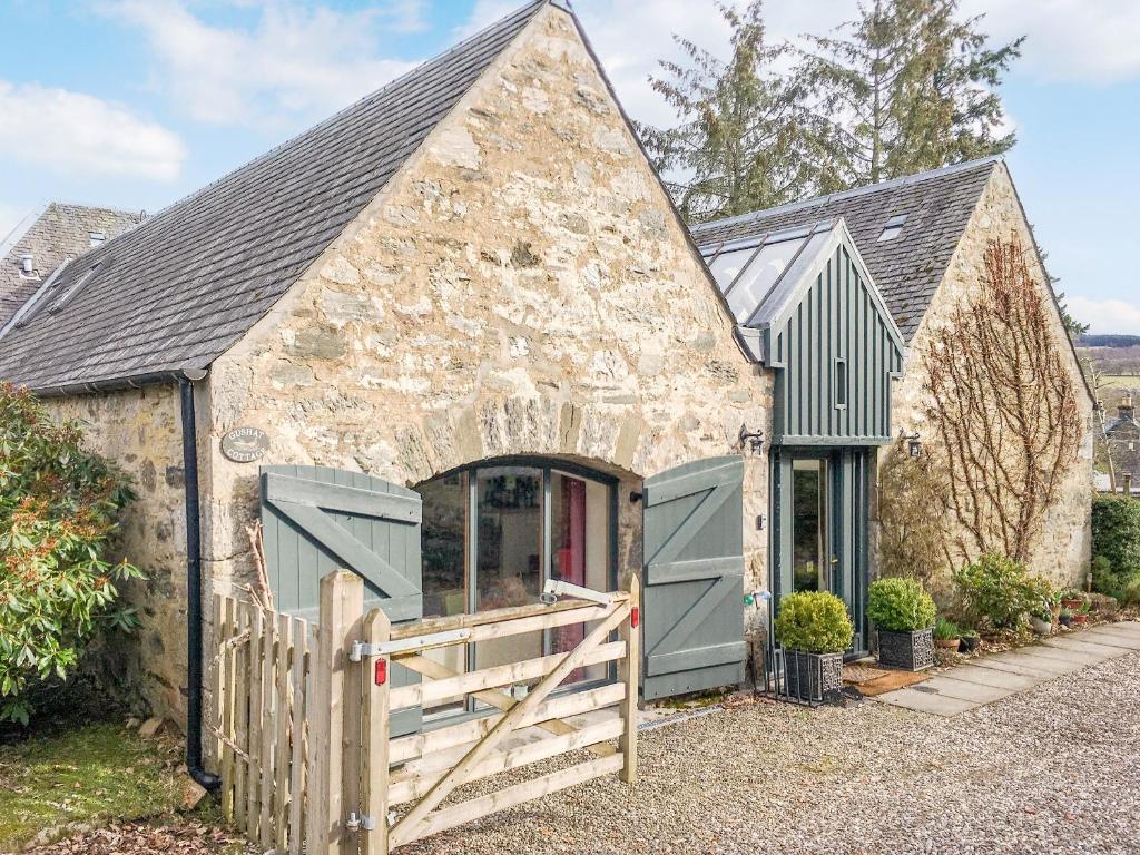 an old stone building with a gate and a barn at Gushat Cottage in Strathtay